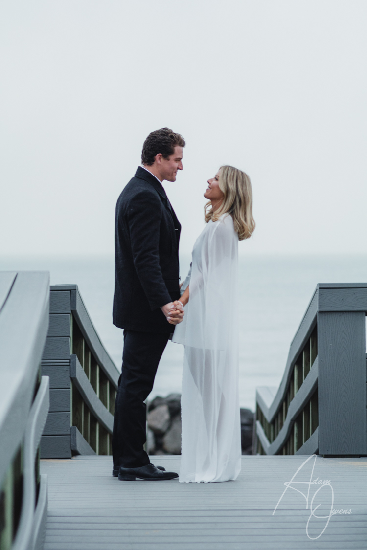 A husband and wife look at each other on a walkway at a beach in front of the ocean